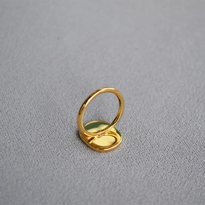 Minimalist gold-plated coconut tree ring with blue enamel inlay on a grey fabric background