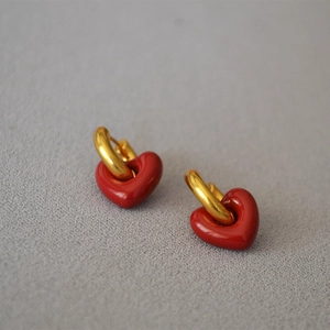 Detail of gold U-shaped hoop earrings with red enamel heart pendants on a textured surface