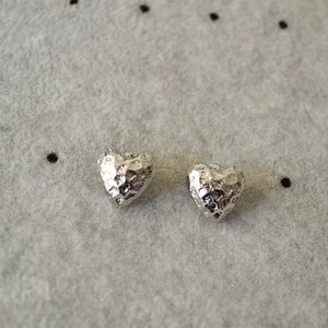 Minimalist silver heart stud earrings with hammered texture on a gray display background