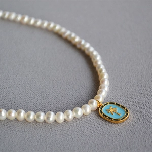 Detailed close-up of freshwater pearl necklace with a blue enamel palm tree pendant