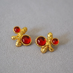Macro shot of vintage gold lava texture earrings with red resin gemstones