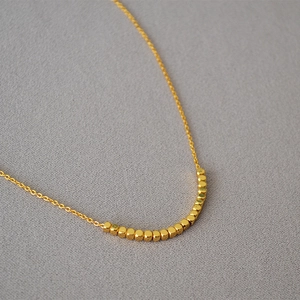 Close-up of minimalist gold-plated brass necklace with small faceted cube beads
