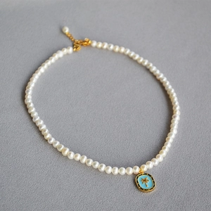 Macro view of a freshwater pearl necklace featuring a blue enamel palm tree pendant detail