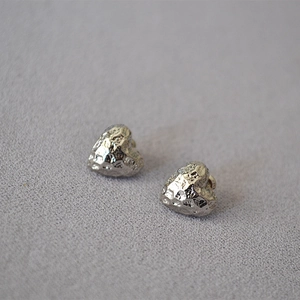 Macro shot of silver heart studs featuring a unique hammered metal texture and glossy finish