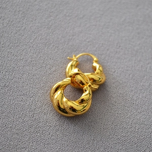 Vue macro détaillée de boucles d'oreilles créoles torsadées dorées sur un tissu texturé