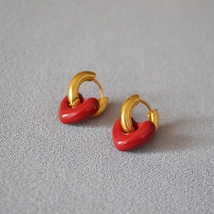 Detail of red enamel heart charms on matte gold-plated hoop earrings against gray background