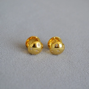 Polished gold brass North Star earrings with cubic zirconia inlay on a grey surface