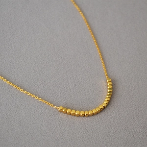 Macro shot of gold-plated square beads on a delicate chain over grey fabric