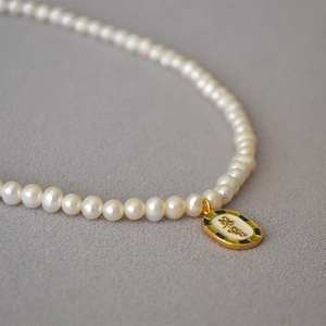 Close-up of vintage freshwater pearl necklace with green enamel grape leaf pendant