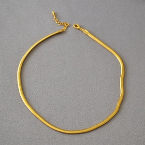 Detail of a golden flat snake chain necklace with lobster clasp and adjustable links