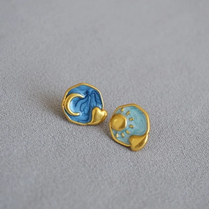 Detail of asymmetric sun and moon enamel earrings with gold stars on textured background