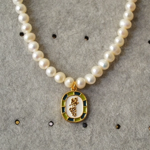 Close-up of freshwater pearl necklace with gold grape motif enamel oval pendant