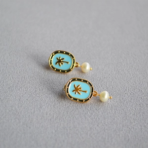 Close-up of gold tropical coconut tree earrings with blue enamel and pearl drops