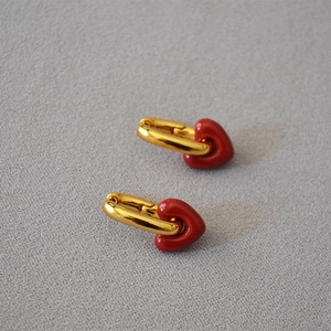 Detail of gold-plated hoop earrings featuring glossy red enamel heart pendants