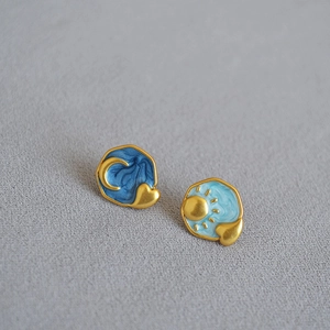 Asymmetric sun and moon enamel stud earrings in blue and gold on a grey fabric base