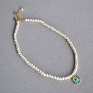 Detailed macro view of tropical palm tree enamel pendant on a natural pearl necklace