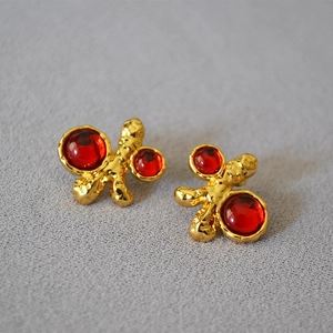 Detail of vintage gold earrings with irregular lava texture and red oval gemstones