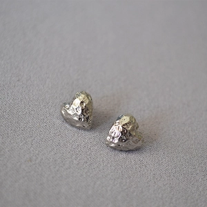 Macro detail of heart-shaped earrings with unique hammered texture and silver finish