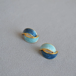 Dettaglio macro di orecchini in smalto blu e ottone dorato con design minimalista