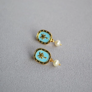 Detail of tropical gold earrings with blue enamel, coconut tree relief and white pearl
