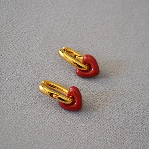 Macro shot of gold oval earrings featuring glossy red enamel heart-shaped charms