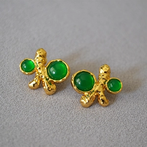 Detail of vintage gold earrings with irregular lava texture and green gemstone inlays