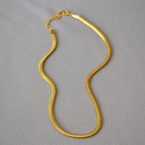 Detailed view of golden snake chain necklace with lobster clasp on grey fabric