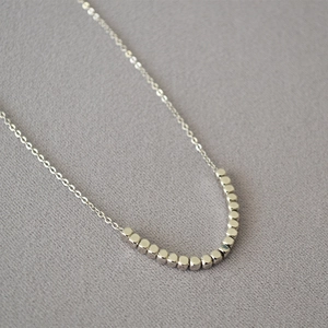 Macro detail of minimalist silver necklace featuring polished square cube metal beads