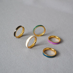 Close-up of five colorful enamel brass gold-plated slim rings arranged on grey fabric