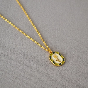 Macro detail of oval enamel pendant with grape motif and gold chain on gray fabric