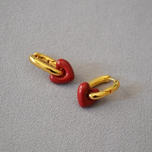Chic gold oval hoop earrings with 3D red enamel heart pendants on a textured background