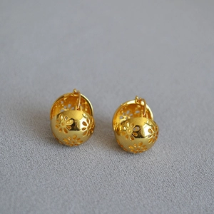 Dettaglio ravvicinato degli orecchini vintage in ottone dorato con motivi floreali cavi