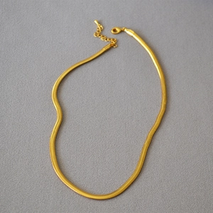 Detail of flat herringbone snake chain with gold plating and lobster clasp on gray fabric
