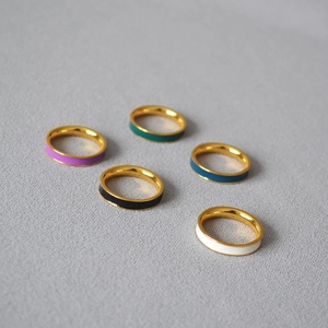 Close-up of five minimalist gold-plated rings with colorful enamel bands on grey fabric