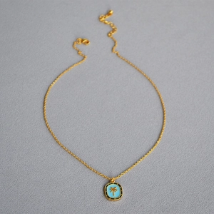 Macro detail of golden palm tree pendant with blue enamel and lobster clasp closure