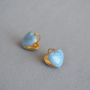 Detail of heart-shaped brass earrings with light blue marbled enamel and gold finish