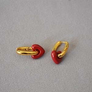 Detailed view of U-shaped gold earrings with polished red heart enamel pendants