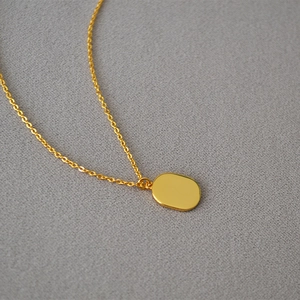 Detailed close-up of a polished gold oval leaf pendant on a delicate chain necklace