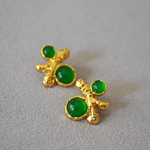 Close-up of irregular gold texture earrings with emerald green gemstones detail
