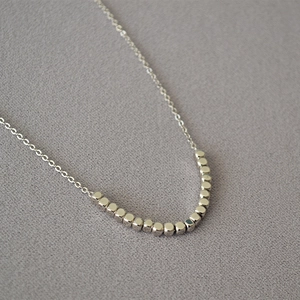 Minimalist silver O-chain necklace featuring small faceted cube metal beads on a grey base