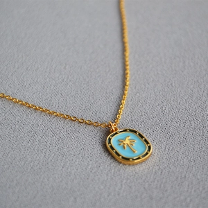 Close-up of golden palm tree on blue enamel oval pendant with irregular pearl chain