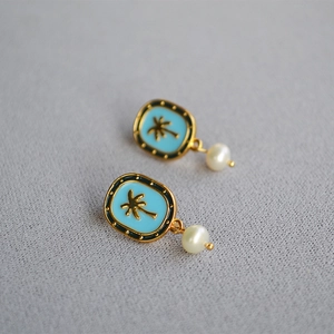 Vintage gold palm tree enamel earrings with hanging white pearls on gray fabric background