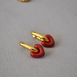 Close-up of golden U-shaped earrings with glossy red heart pendants on gray background