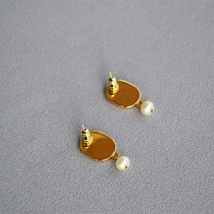 Detail shot of vintage gold oval earrings with hanging white pearls on gray texture