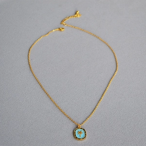 Detailed close-up of a blue enamel coconut palm pendant with irregular pearl necklace