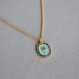 Detail view of blue enamel palm tree pendant on golden freshwater pearl necklace