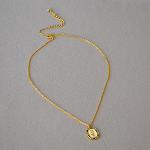 Detail of vintage gold necklace with white enamel floral pendant on grey fabric