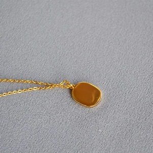 Macro shot of polished gold rectangular pendant and fine chain on dark textured fabric
