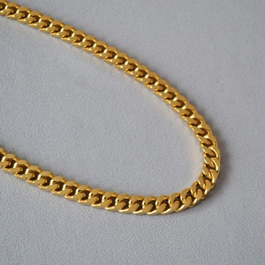 Close-up of polished gold Cuban link chain necklace on a gray textured background