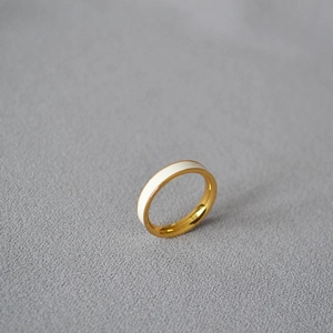 Macro shot of gold plated brass ring with white enamel coating on a textured surface